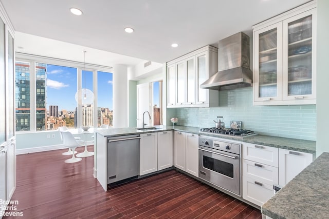 kitchen featuring sink, appliances with stainless steel finishes, white cabinetry, decorative light fixtures, and wall chimney exhaust hood