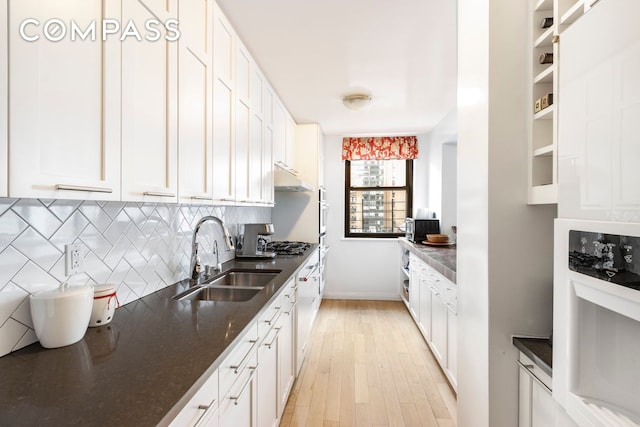 kitchen with a sink, under cabinet range hood, white cabinetry, tasteful backsplash, and light wood-type flooring