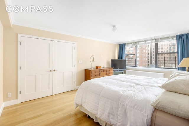 bedroom featuring light wood-style flooring, baseboards, a closet, and ornamental molding