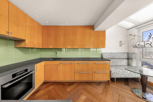 kitchen with dark countertops, cooktop, stainless steel oven, a sink, and under cabinet range hood