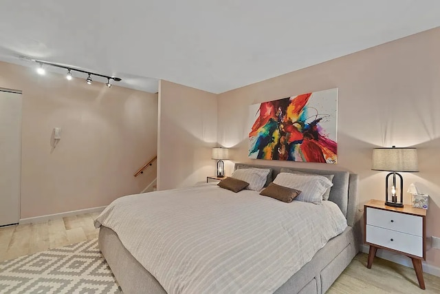 bedroom featuring wood finished floors, rail lighting, and baseboards