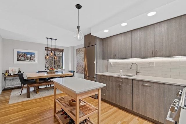 kitchen featuring decorative light fixtures, stainless steel built in fridge, tasteful backsplash, sink, and light wood-type flooring