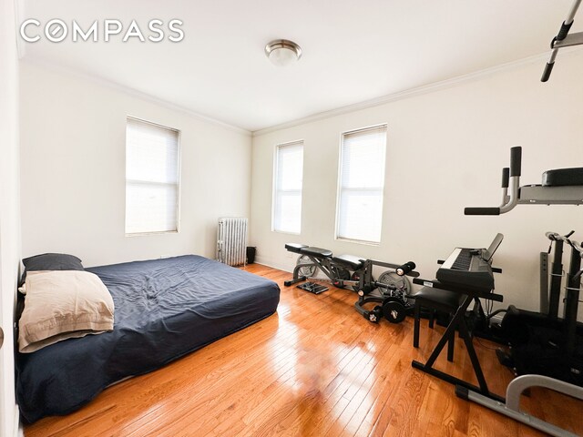 bedroom with multiple windows, wood-type flooring, radiator, and ornamental molding