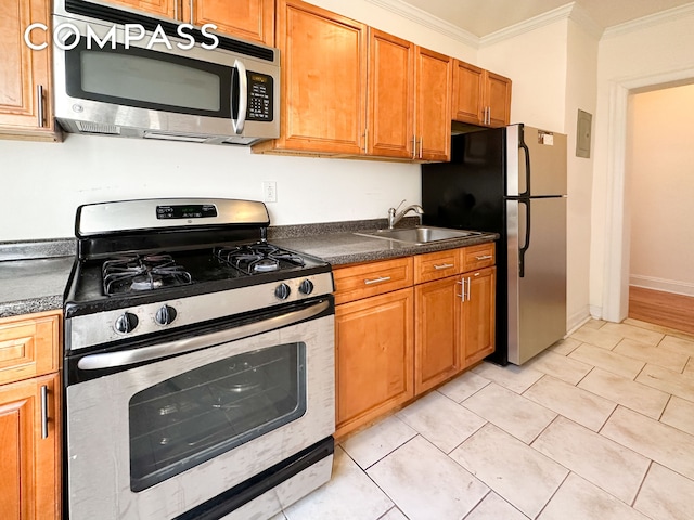 kitchen featuring a sink, appliances with stainless steel finishes, brown cabinetry, dark countertops, and crown molding