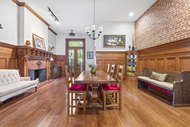 dining space featuring brick wall, track lighting, a chandelier, light hardwood / wood-style flooring, and crown molding