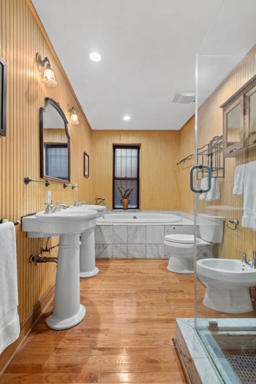 bathroom featuring a tub, toilet, wood walls, hardwood / wood-style flooring, and a bidet