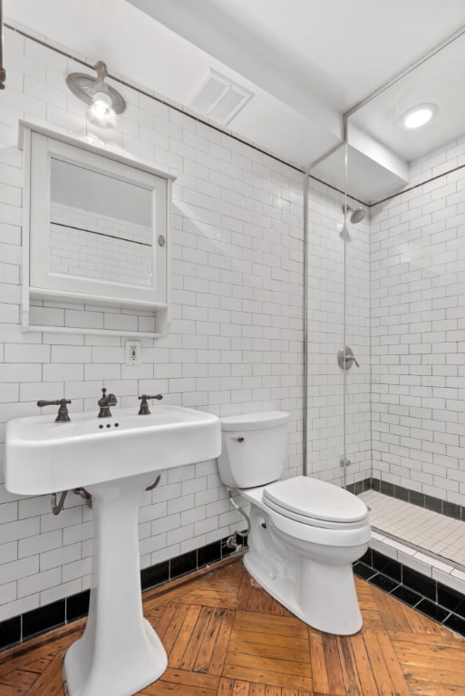 bathroom featuring tile walls, toilet, a tile shower, and parquet floors