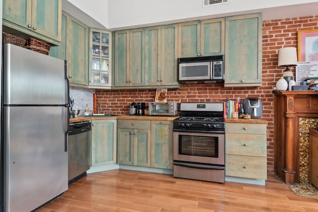 kitchen with wooden counters, green cabinets, light hardwood / wood-style flooring, backsplash, and stainless steel appliances