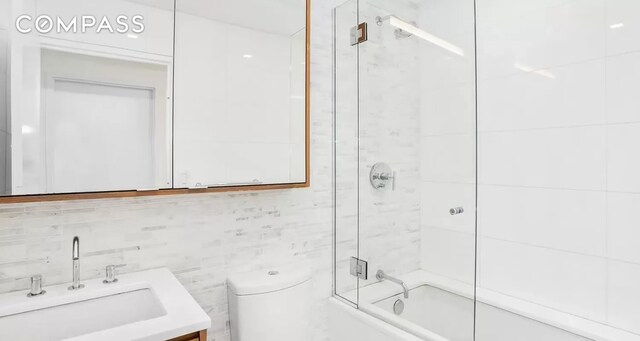 full bathroom featuring enclosed tub / shower combo, toilet, tile walls, and vanity