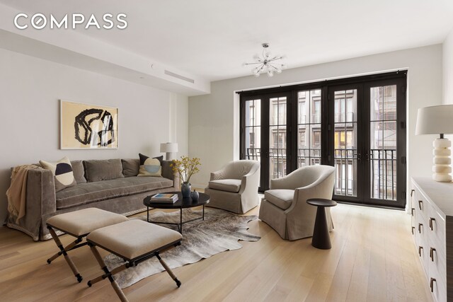 living room with light wood-type flooring, french doors, and a notable chandelier