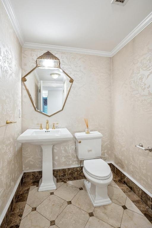 bathroom with tile patterned flooring, toilet, baseboards, ornamental molding, and wallpapered walls