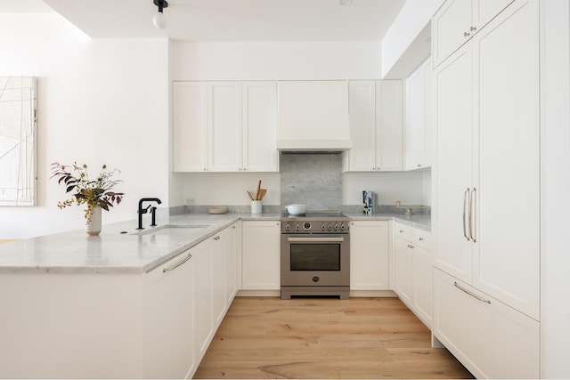 kitchen with a peninsula, white cabinetry, high end range, and a sink