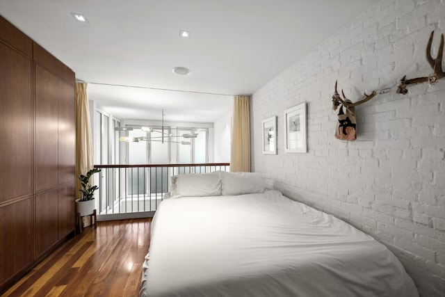 unfurnished bedroom featuring dark hardwood / wood-style flooring, a notable chandelier, and brick wall