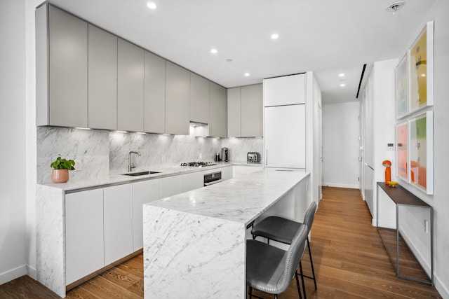 kitchen with wood finished floors, a sink, modern cabinets, backsplash, and a kitchen island