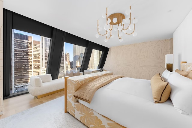 bedroom with a view of city, a notable chandelier, light wood-style floors, a wall of windows, and wallpapered walls