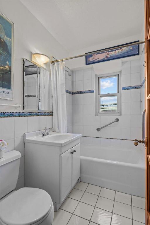 full bathroom with tile patterned floors, toilet, tile walls, vanity, and shower / bathtub combination with curtain