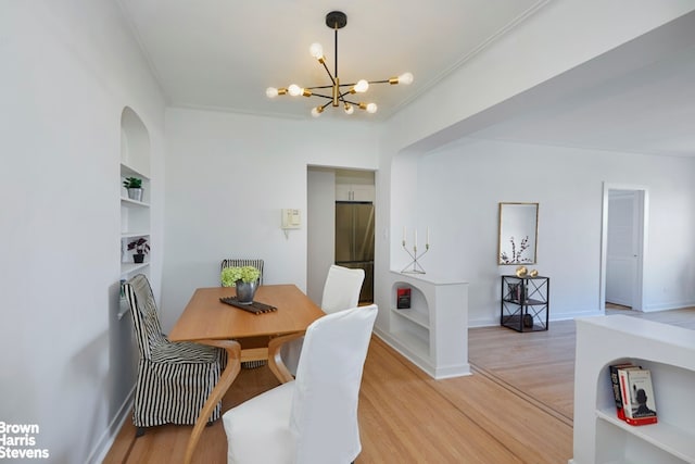 dining space featuring light wood finished floors, baseboards, built in features, an inviting chandelier, and crown molding