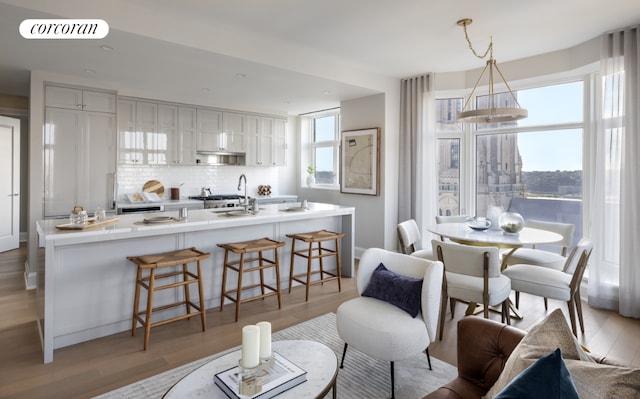 kitchen with sink, light wood-type flooring, a kitchen breakfast bar, pendant lighting, and decorative backsplash