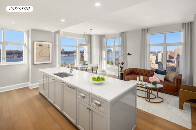 kitchen featuring sink, light stone counters, a water view, a center island with sink, and light hardwood / wood-style flooring