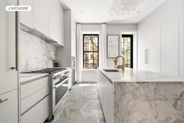 kitchen with modern cabinets, a sink, stainless steel stove, and light stone countertops