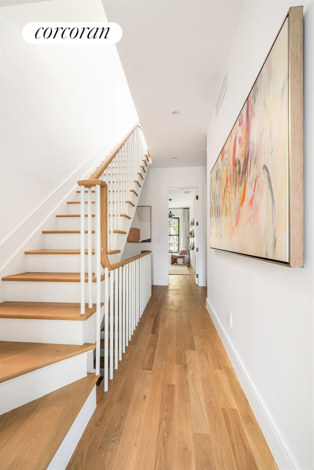 corridor featuring stairs, wood finished floors, visible vents, and baseboards