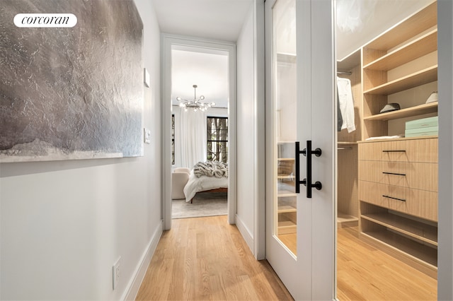 hallway featuring light wood-style floors, a notable chandelier, and baseboards