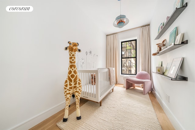 bedroom featuring visible vents, a nursery area, light wood-style flooring, and baseboards