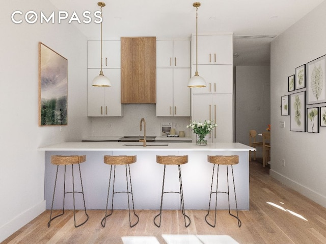 kitchen with white cabinetry, sink, decorative light fixtures, and a kitchen breakfast bar