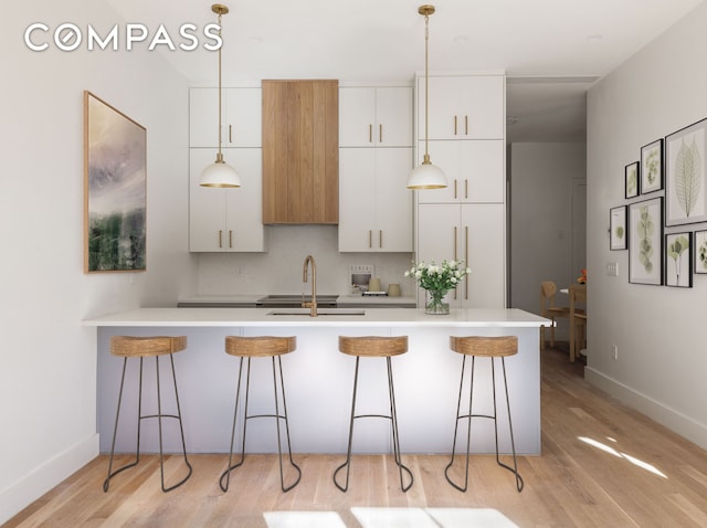 kitchen featuring a breakfast bar area, light wood-style flooring, a sink, light countertops, and white cabinetry