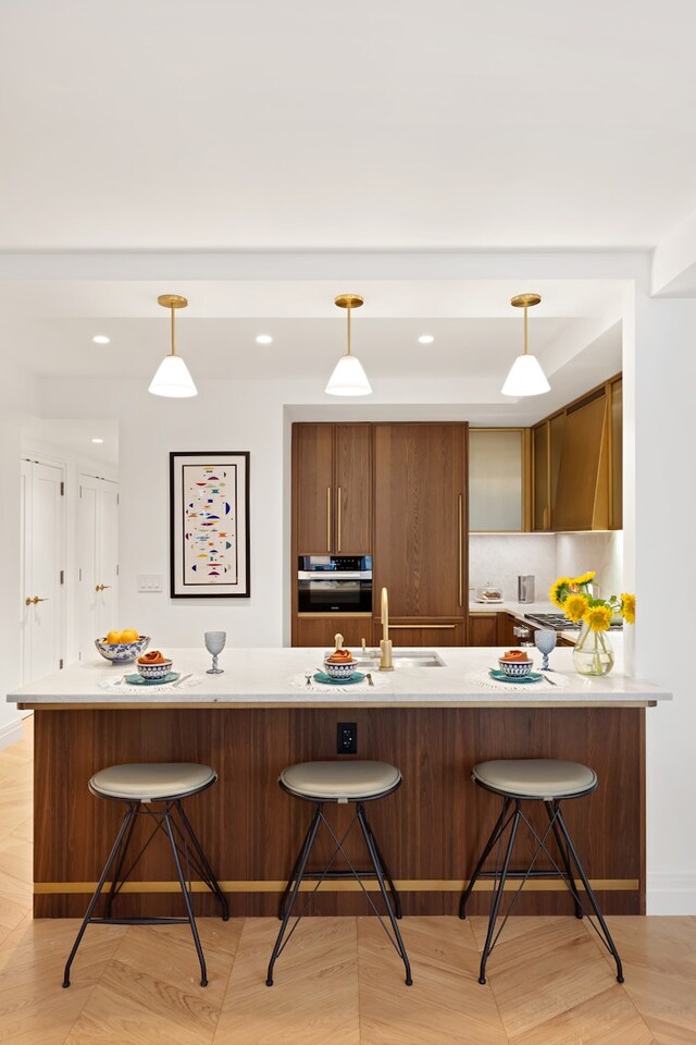 kitchen with a breakfast bar, a sink, hanging light fixtures, light countertops, and wall oven