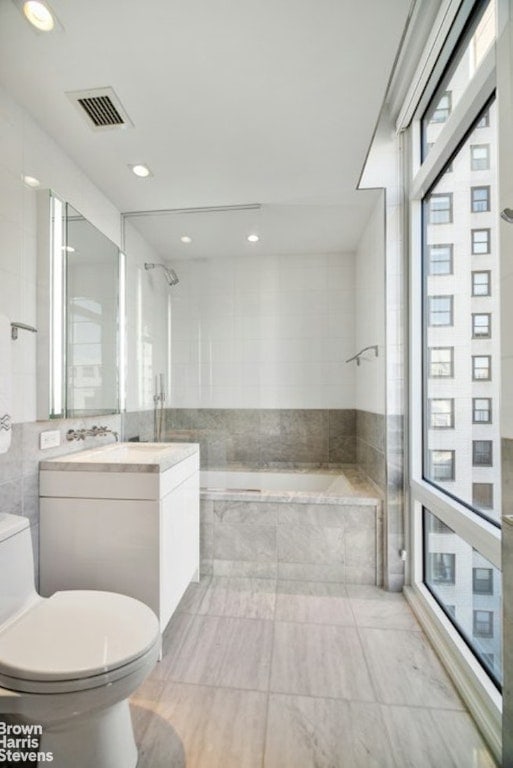 full bathroom with toilet, vanity, tile walls, and tiled shower / bath