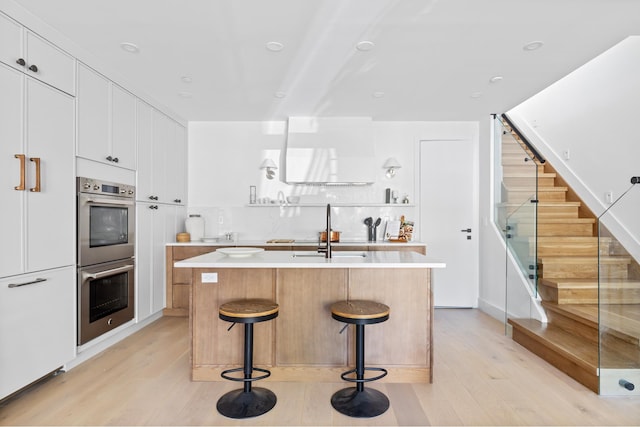 kitchen featuring light countertops, light wood finished floors, stainless steel double oven, and a sink