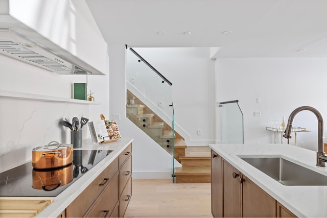 134 Weirfield St Unit 2, New York City, NY 11221 - kitchen featuring wall chimney range hood, a sink, light wood finished floors, black electric cooktop, and light stone countertops