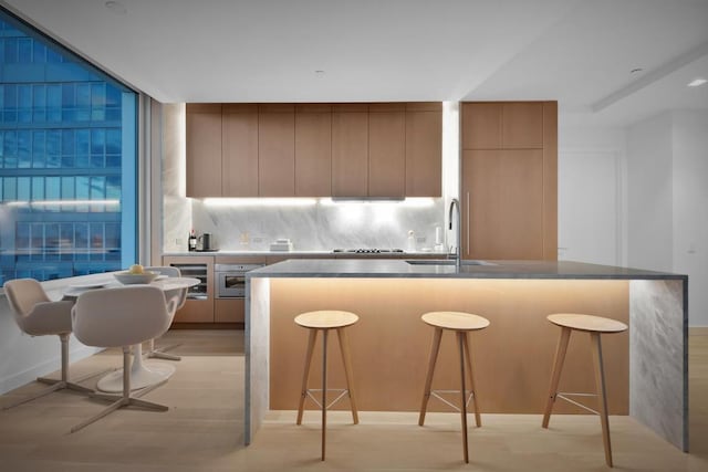 kitchen featuring light hardwood / wood-style floors, decorative backsplash, a kitchen island with sink, a breakfast bar, and sink