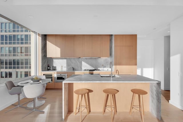 kitchen with decorative backsplash, sink, a breakfast bar area, and light hardwood / wood-style floors