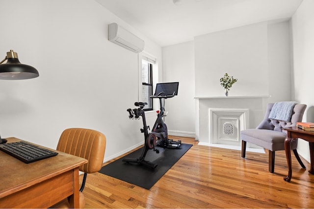 exercise area with a wall mounted air conditioner, wood finished floors, and baseboards