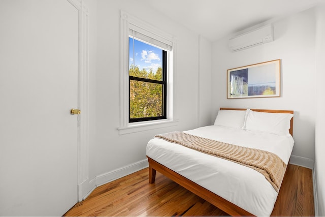 bedroom with wood finished floors, baseboards, and a wall mounted AC