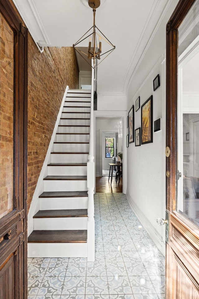 interior space featuring a chandelier, brick wall, ornamental molding, and baseboards