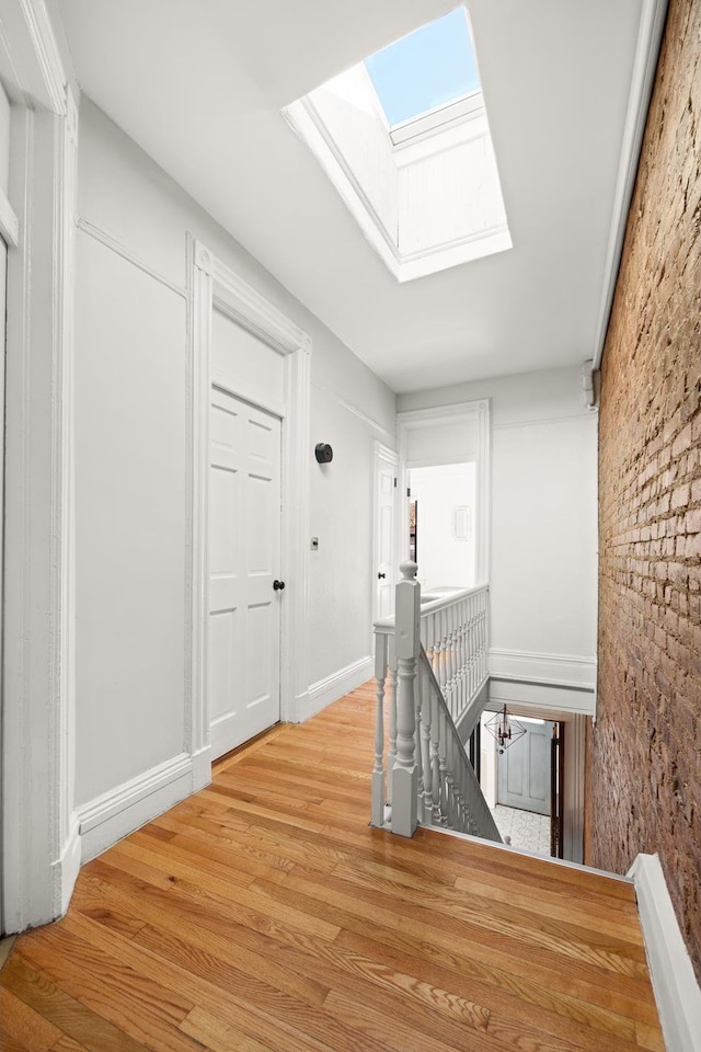 corridor featuring a skylight, baseboards, an upstairs landing, and wood finished floors