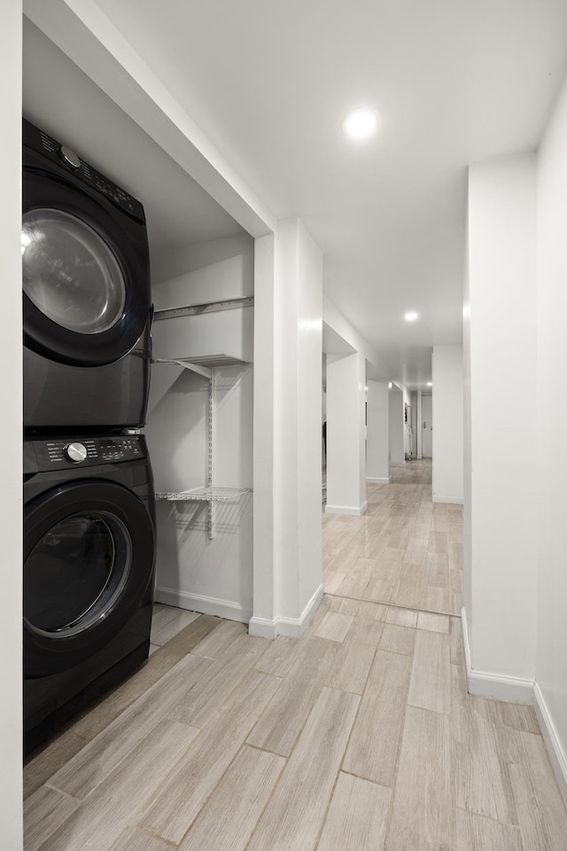 laundry area featuring laundry area, stacked washer / dryer, wood finished floors, and baseboards