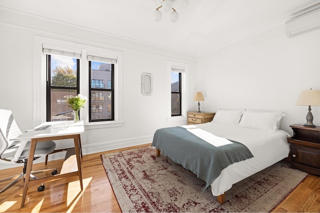 bedroom featuring baseboards, a wall mounted air conditioner, crown molding, and light wood finished floors