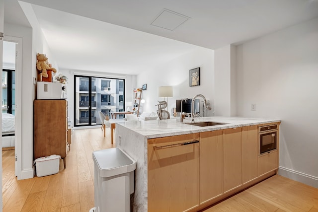 kitchen with kitchen peninsula, light wood-type flooring, light stone countertops, and sink