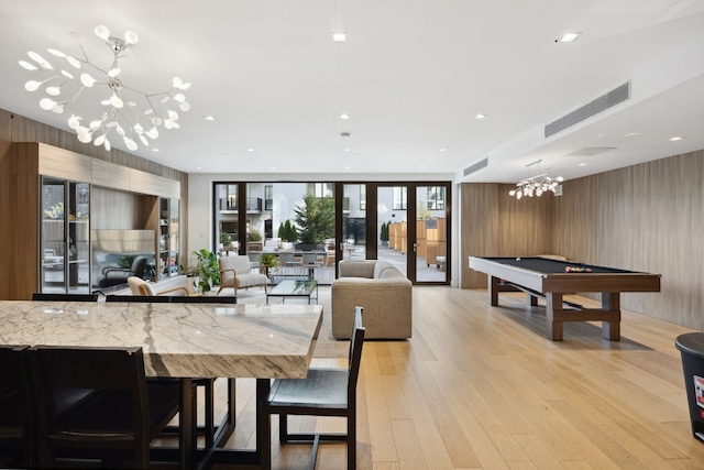 dining room featuring french doors, billiards, wood walls, an inviting chandelier, and light hardwood / wood-style flooring