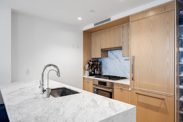 kitchen with light brown cabinetry, sink, a kitchen island with sink, light stone counters, and stainless steel appliances