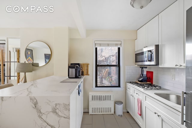 kitchen featuring radiator, beam ceiling, stainless steel appliances, decorative backsplash, and white cabinets