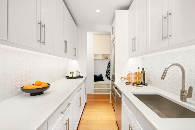 kitchen with a sink, light wood finished floors, tasteful backsplash, and white cabinets