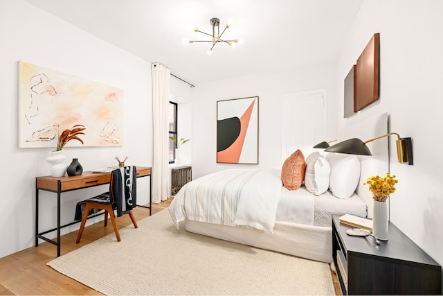 bedroom featuring a notable chandelier, radiator heating unit, and wood finished floors