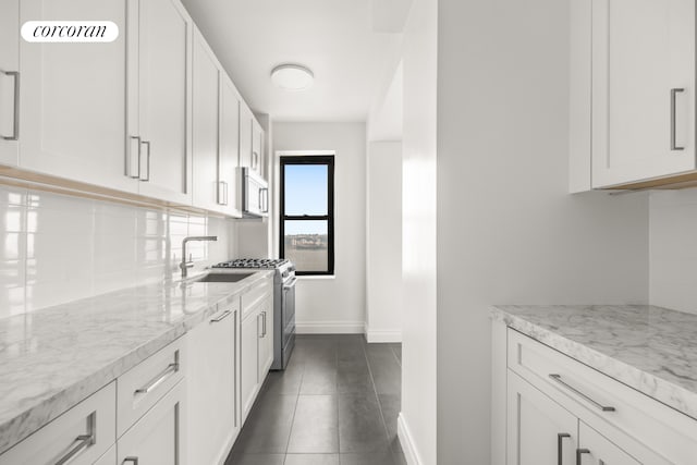 kitchen featuring a sink, baseboards, light stone counters, decorative backsplash, and white cabinets