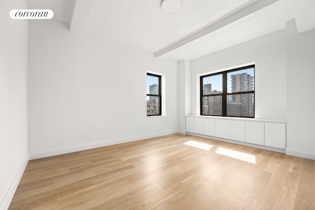 unfurnished room with beamed ceiling and light wood-type flooring