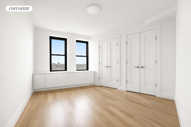 unfurnished bedroom with two closets, light wood finished floors, and baseboards